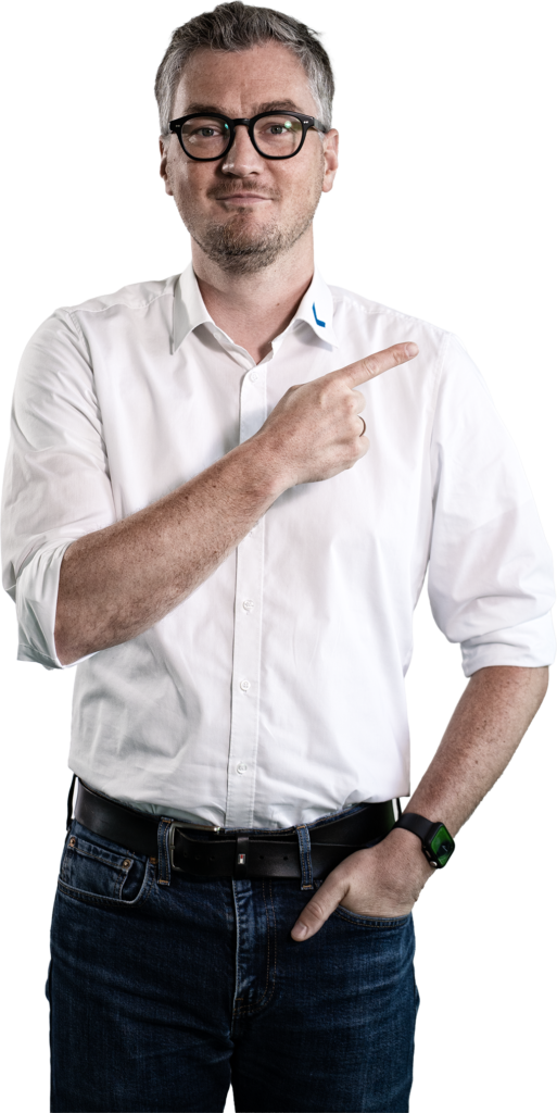 Un hombre con camisa blanca y vaqueros señala con el dedo hacia un lado.