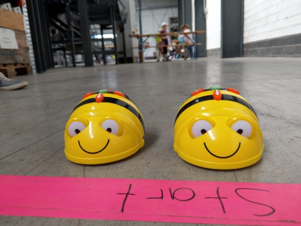 Dos robots amarillos con forma de abeja situados en un punto de partida dentro de una nave.