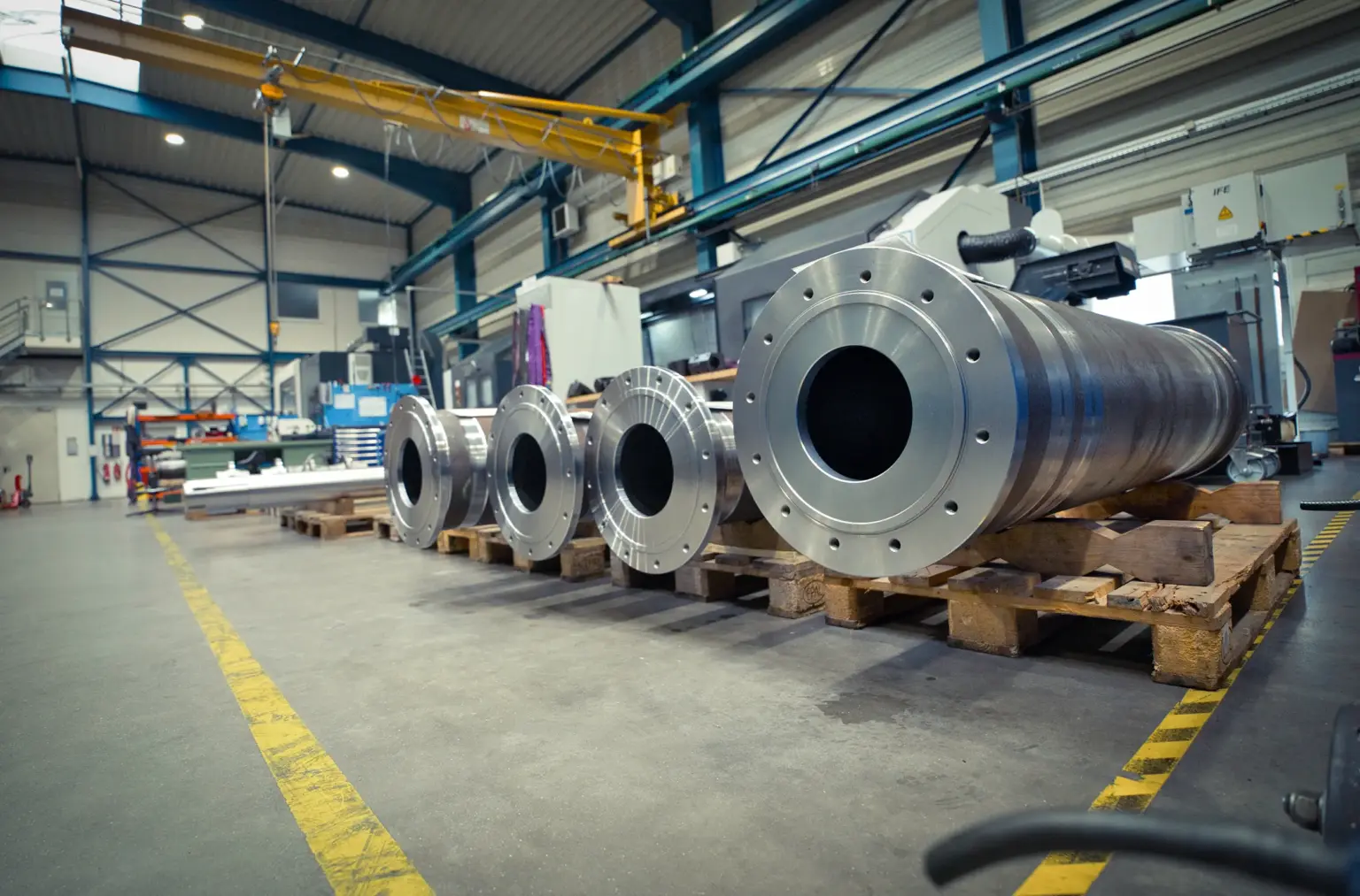Grandes cilindros metálicos sobre palés en una nave industrial dedicada al mecanizado CNC de piezas de gran tamaño.