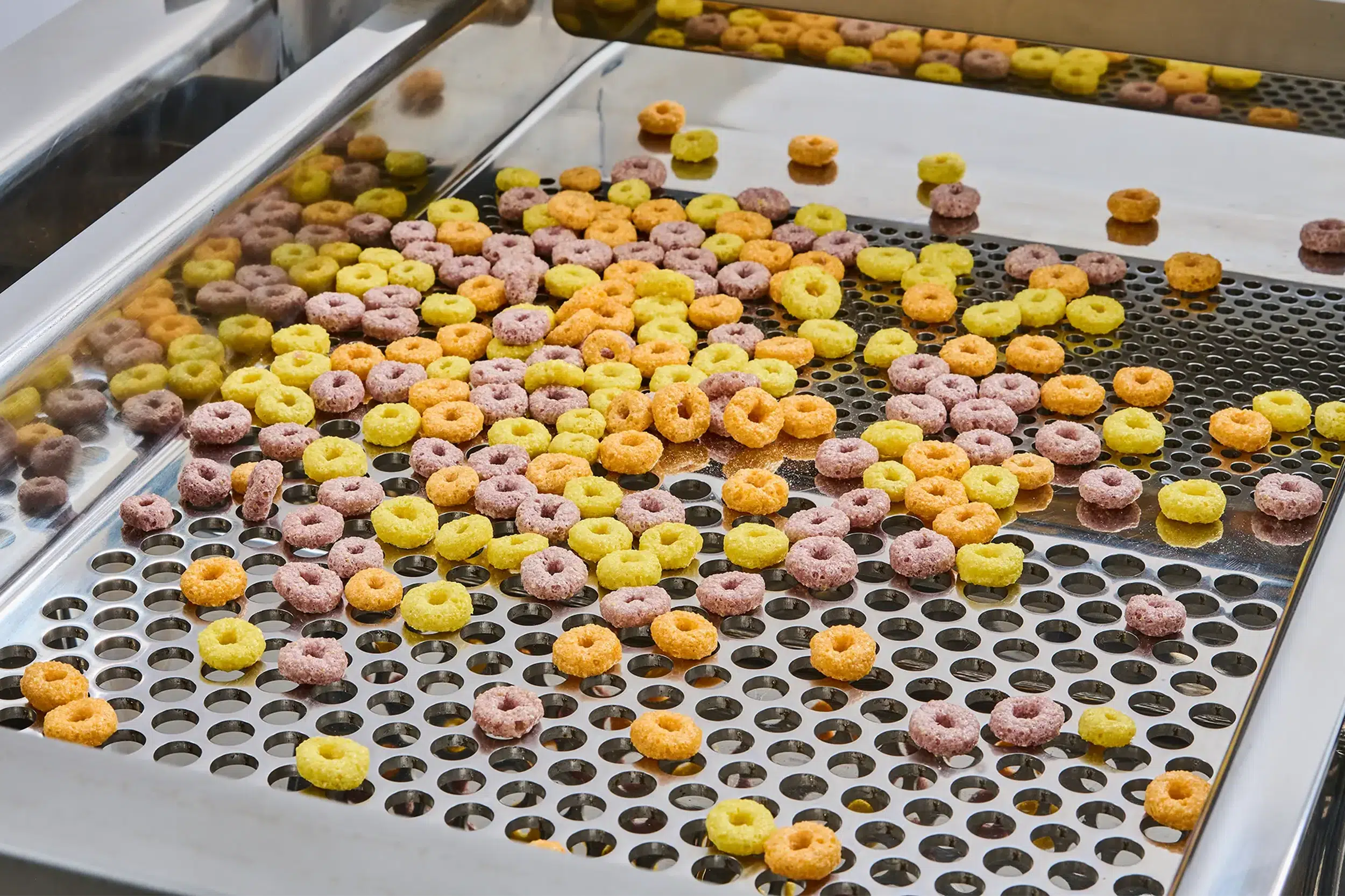 Las cribadoras de alimentos separan los anillos de cereales de distintos colores sobre una criba.
