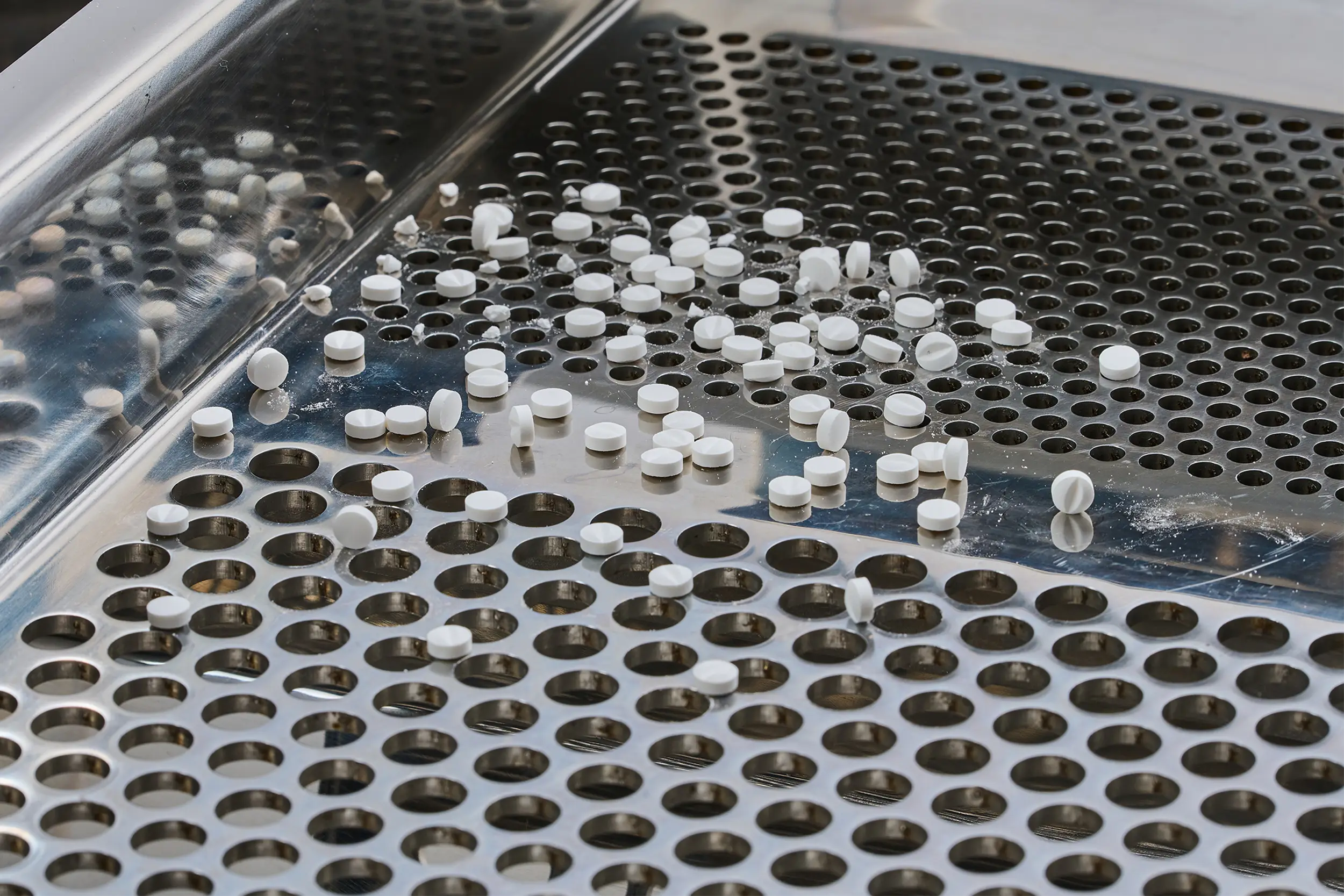 Comprimidos blancos sobre un tamiz metálico en una tamizadora farmacéutica.