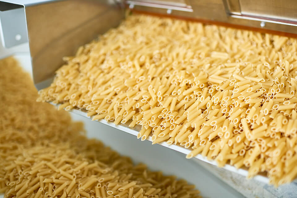 Pasta en una canaleta vibratoria dentro de una línea de producción.