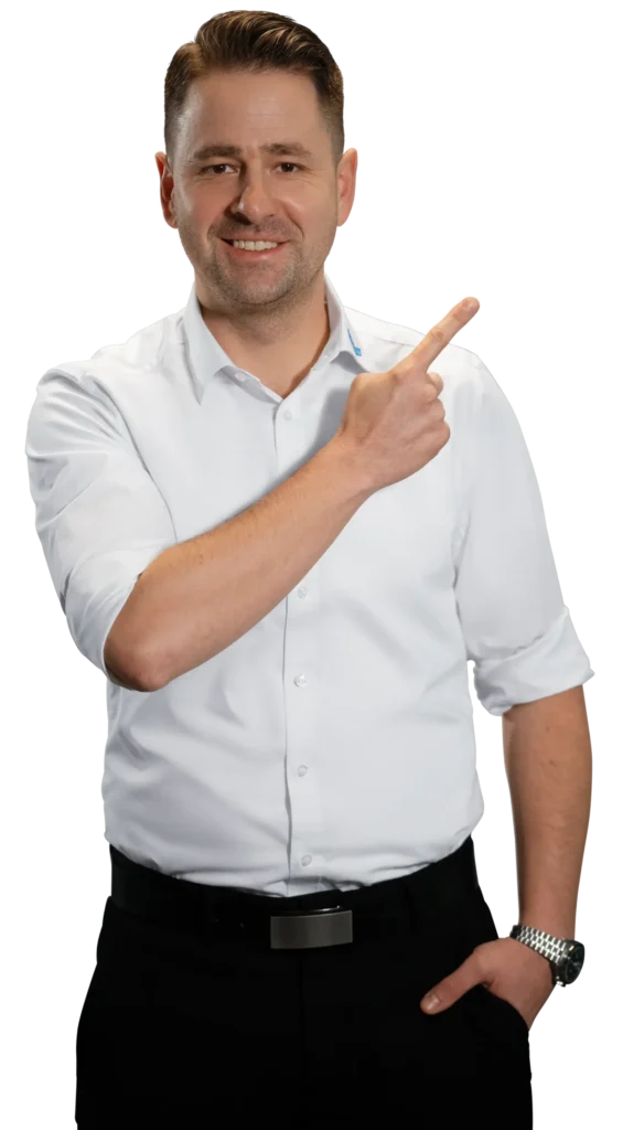 Un hombre con camisa blanca señala hacia un lado con una sonrisa.