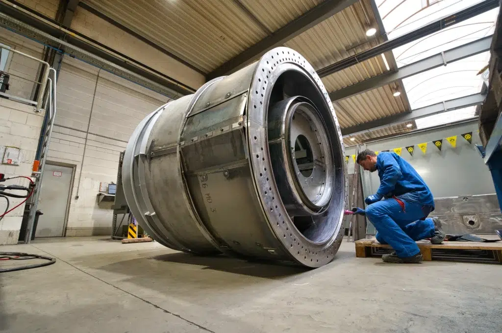 SPALECK, un técnico en construcción mecánica, está arrodillado junto a un gran conjunto soldado y monta piezas. Este subconjunto forma parte de un gran conjunto soldado destinado a una turbina de gas. La imagen muestra el proceso de producción en SPALECK.
