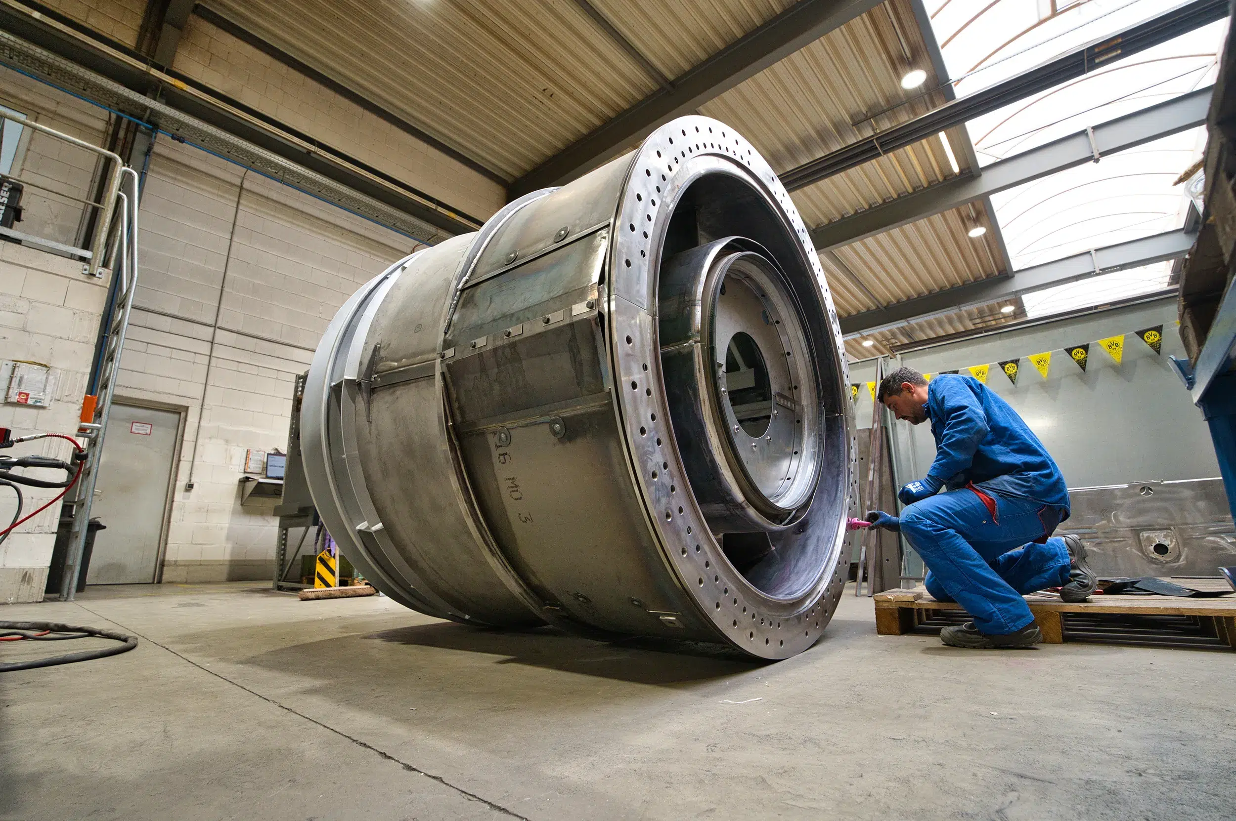 SPALECK, un técnico en construcción mecánica, está arrodillado junto a un gran conjunto soldado y monta piezas. Este subconjunto forma parte de un gran conjunto soldado destinado a una turbina de gas. La imagen muestra el proceso de producción en SPALECK.