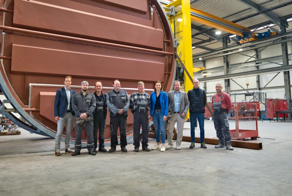 Un grupo de personas está delante de una gran máquina industrial en la nave de la fábrica.