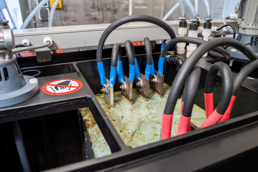 Primer plano de un equipo de electrocoagulación en funcionamiento. Muestra las láminas eléctricas en el agua contaminada.