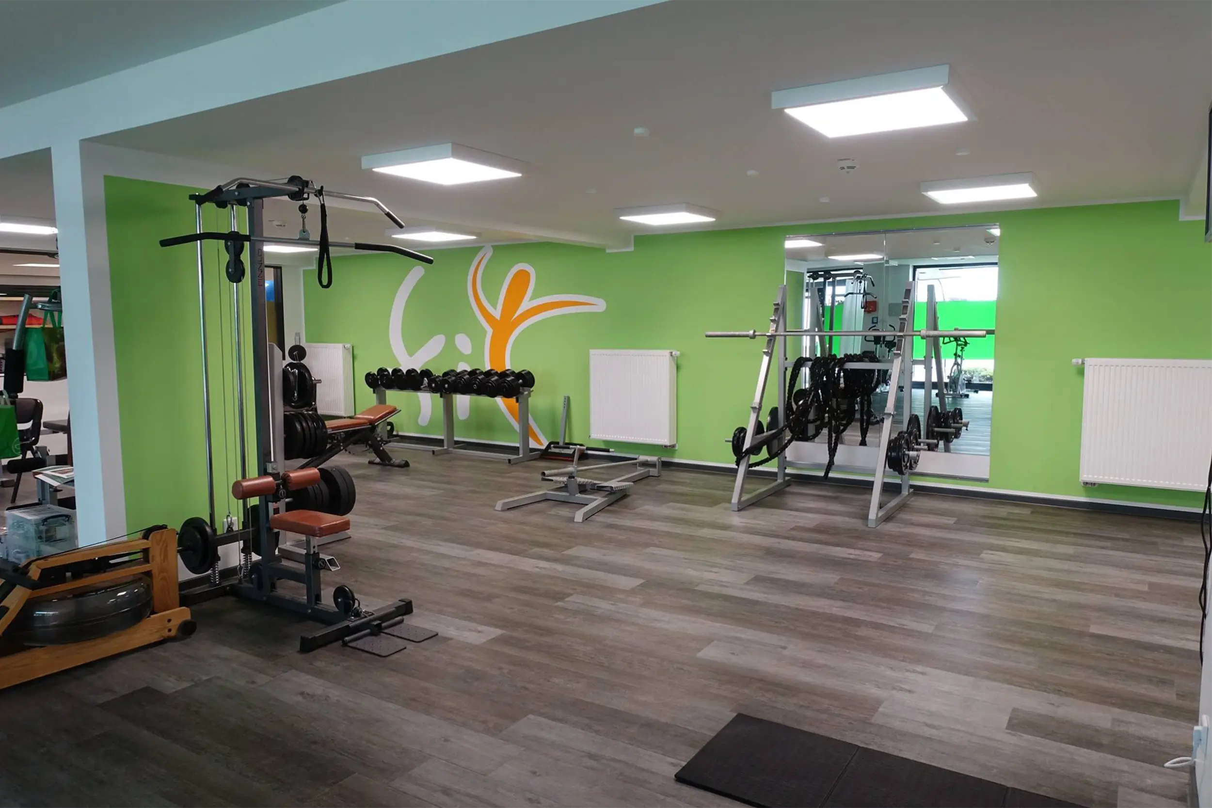 Moderner Fitnessraum mit Kraftgeräten und grüner Wand.