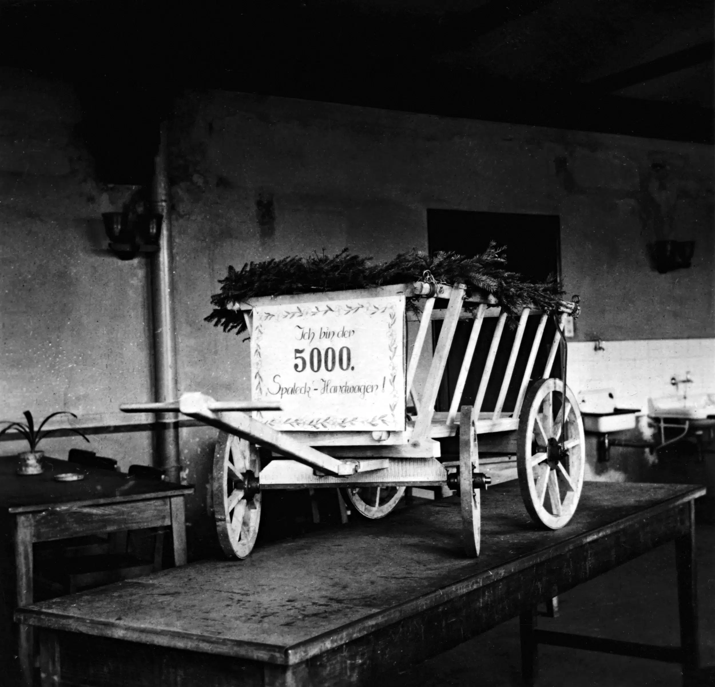 Holzwagen mit Schild 'Ich bin der 5000. Spende-Hackwagen' auf einem Tisch.
