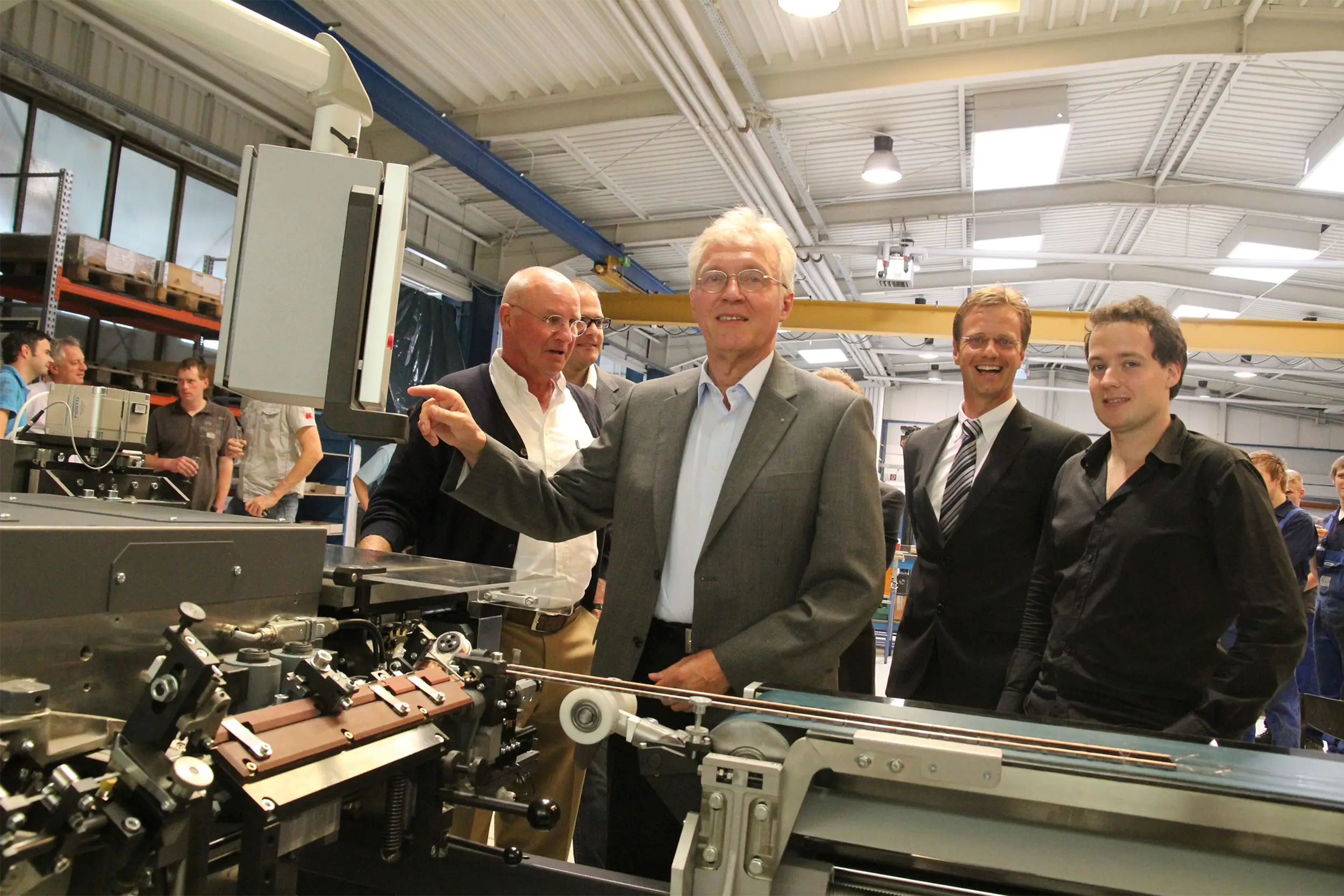 Gruppe von Männern in einer Fabrikhalle neben einer Maschine.