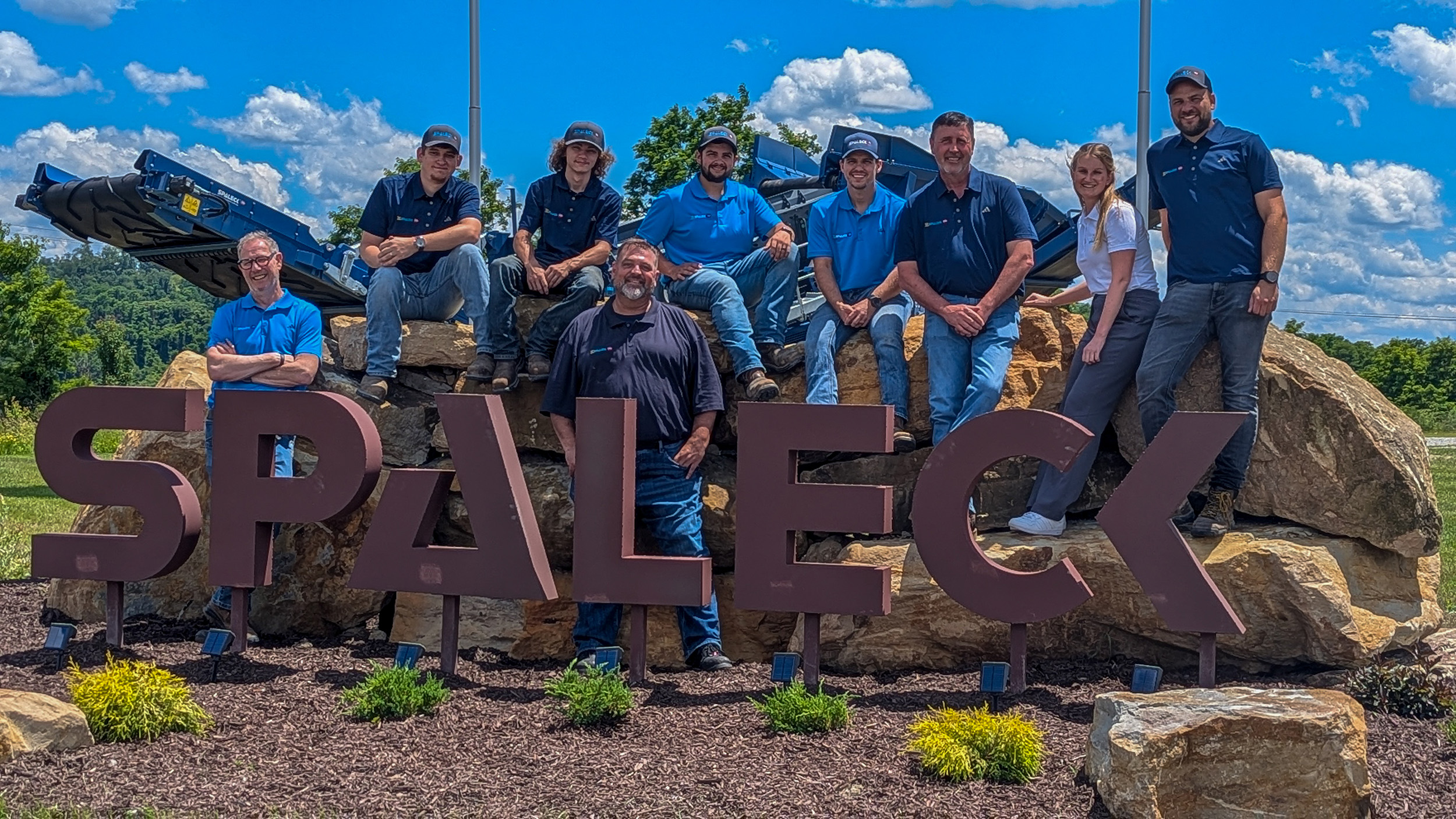 Foto de equipo de Spaleck USA junto al logotipo de Spaleck en Charleroi, con motivo de la inauguración de las instalaciones y bajo un cielo azul